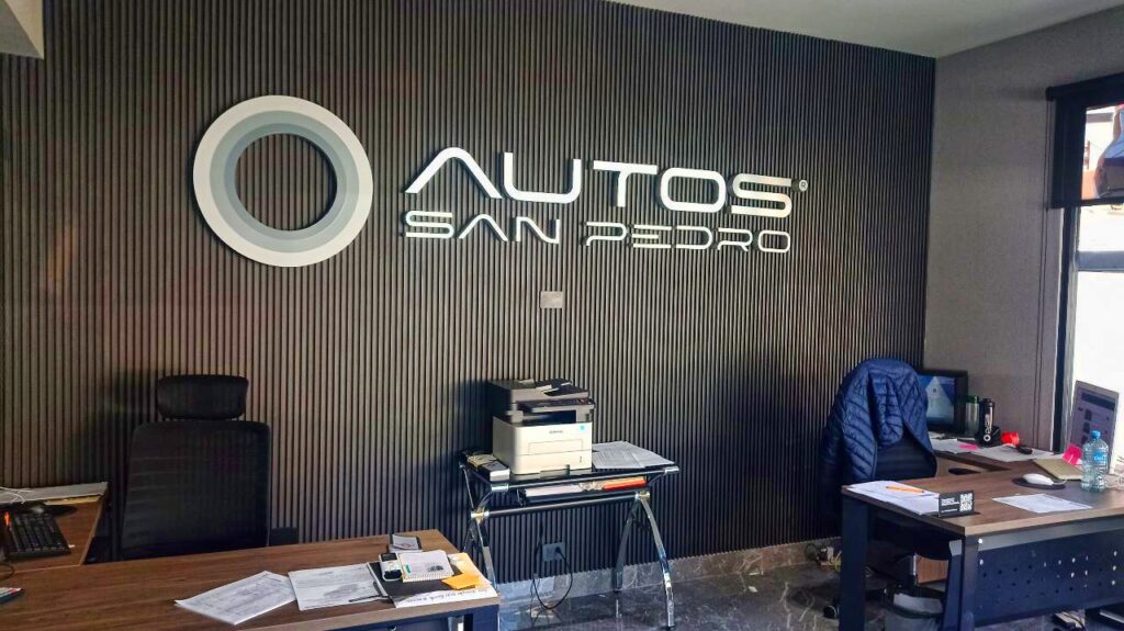 Identidad corporativa de pared con acabado metálico y luz indirecta instalada sobre panel de madera decorativo.