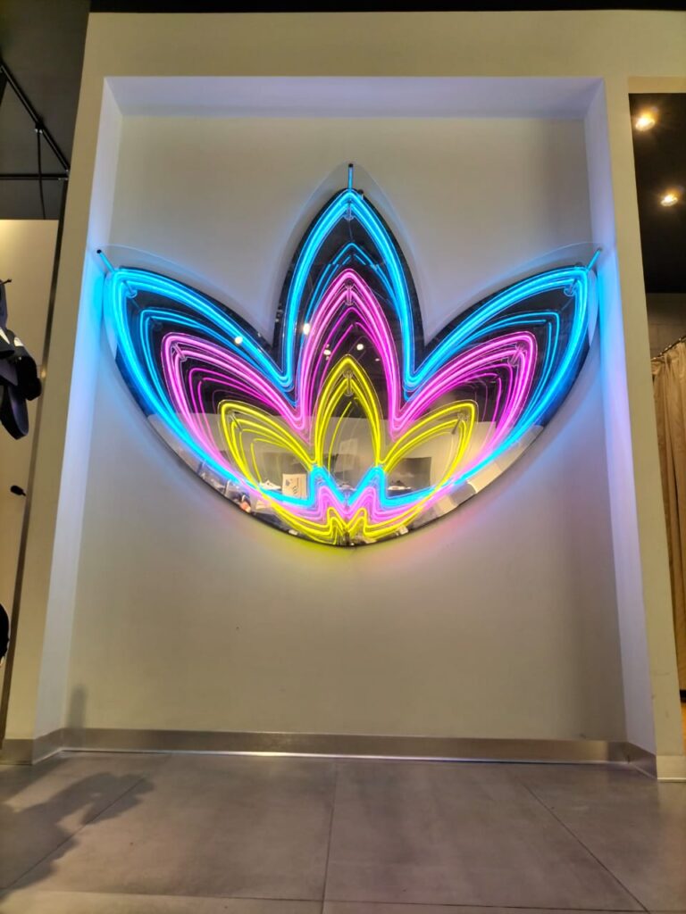 Logotipo de pared en acrílico con capas múltiples e iluminación LED de colores neón cian, magenta y amarillo.